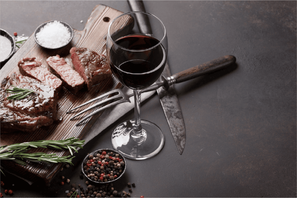 Red wine next to a steak on cutting board with herbs and spices