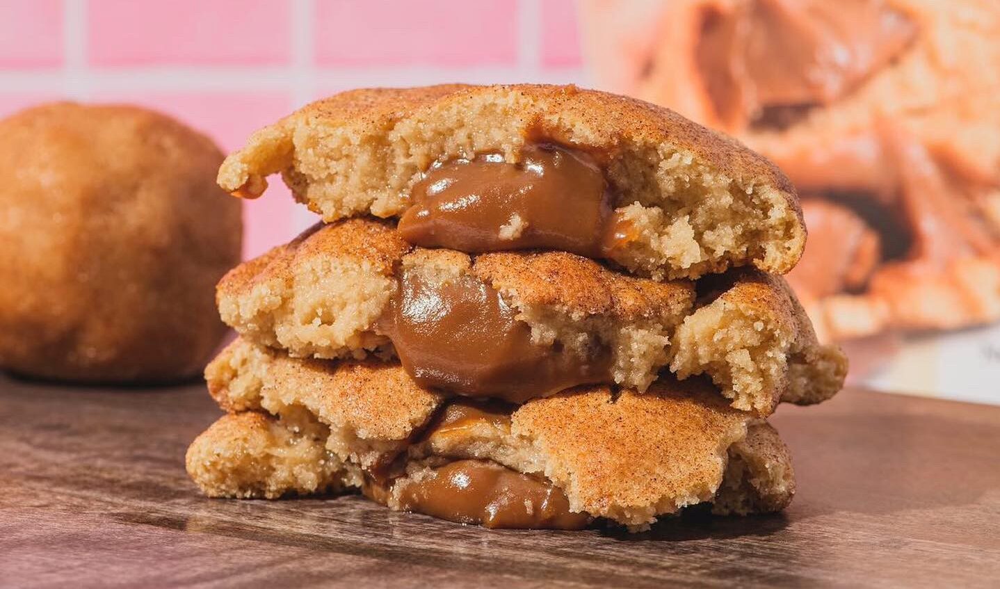 La Gringuita cookie broken in half on a kitchen counter with gooey caramel dripping out of the middle of the cookie stack