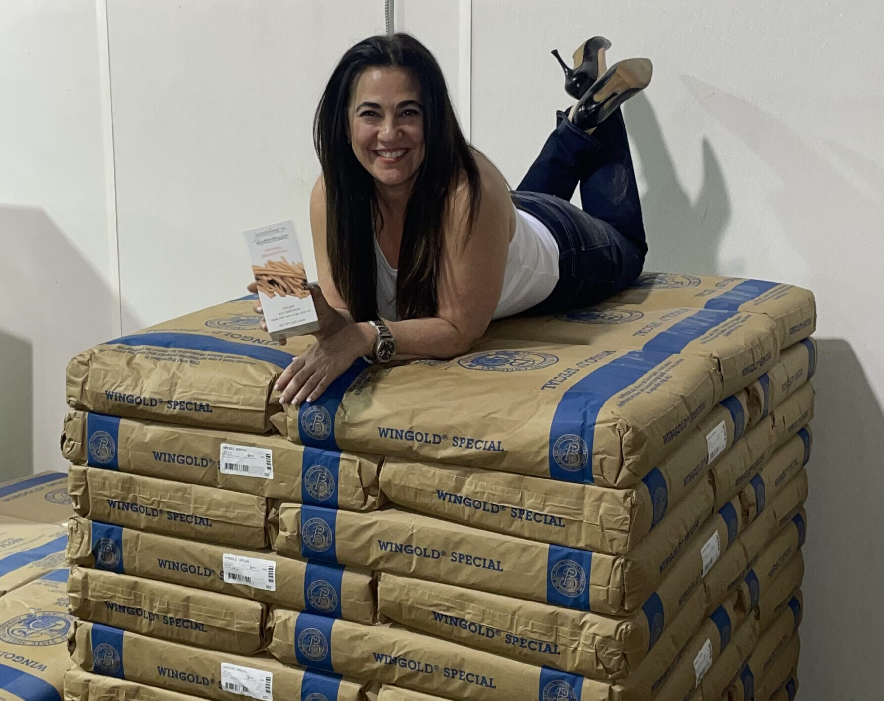 Jennifer laying on a pallet of flour holding a box of her homemade breadsticks and flatbreads