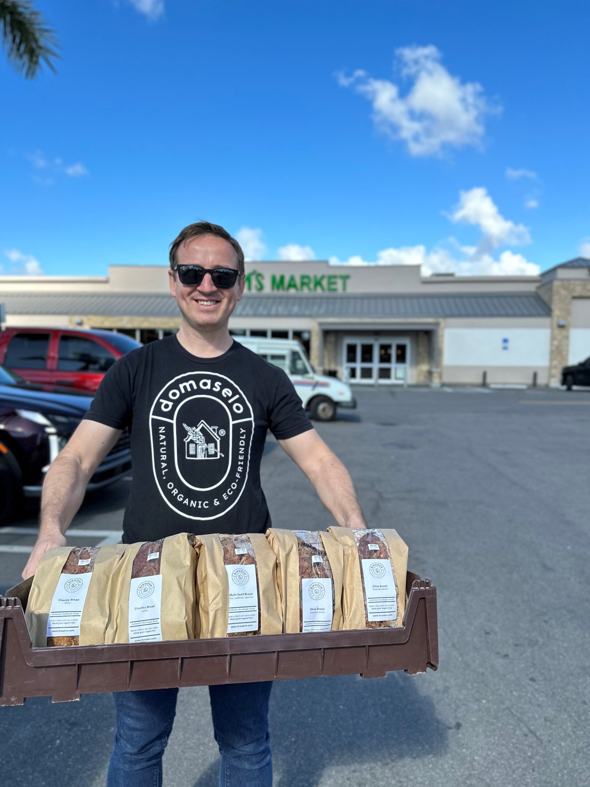 Emil of Domaselo bread carrying a box of packaged breads in the Milam's Markets parking lot