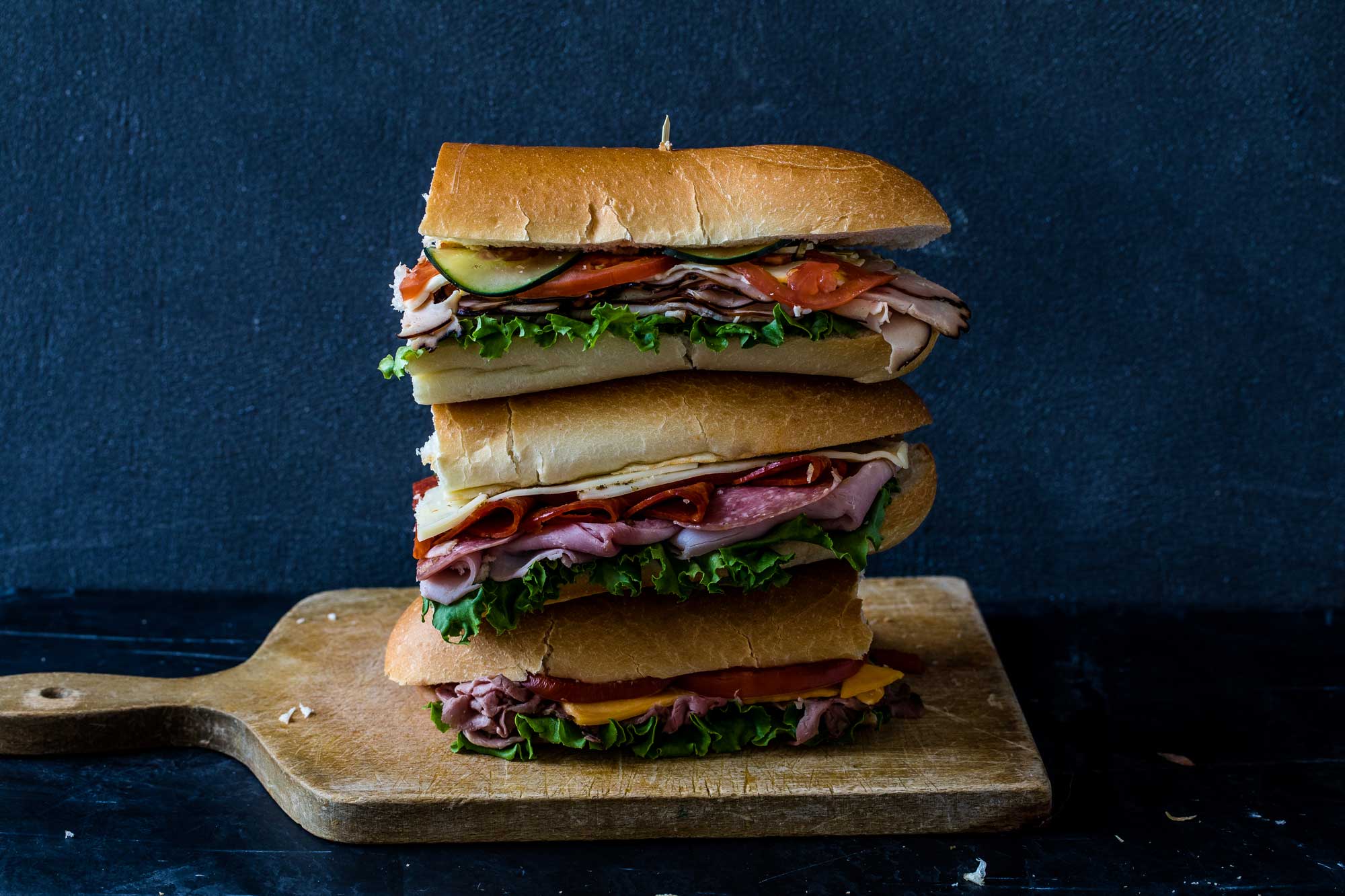 a stack of sub sandwiches piled on a cutting board