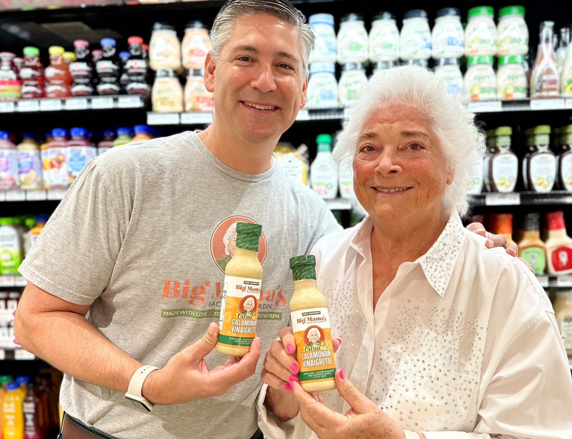 Lois Marks and Ethan Shapiro holiding Big Mama's Calamondin Vinaigrette in the grocery store aisle